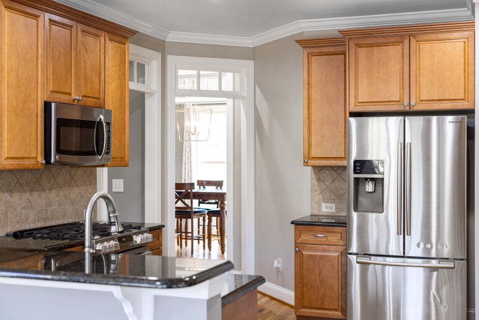 A spacious modern kitchen featuring wooden cabinets, a stainless steel refrigerator, and a sleek microwave.